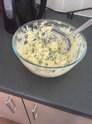 Cheese and spinach uncooked muffin mixture in a clear bowl on a grey worktop